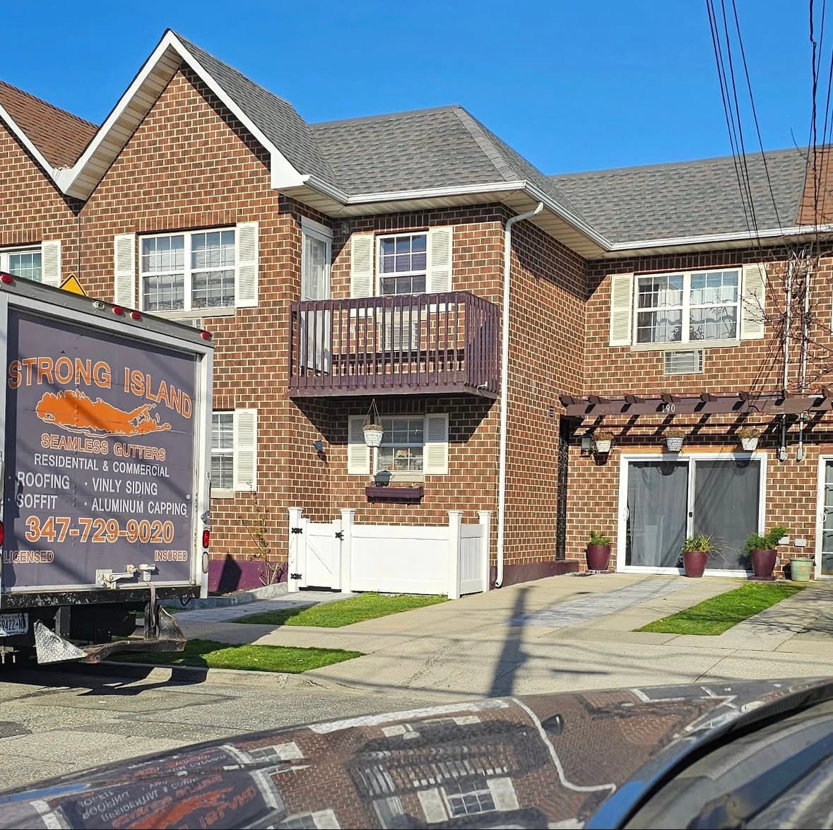 The company box truck parked in front of a brick home fitted with new white seamless gutters and leaders.